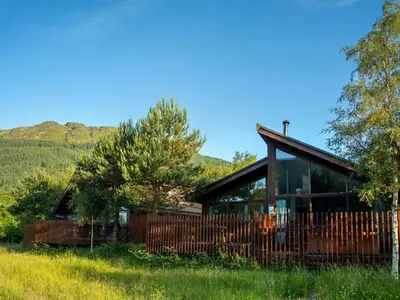 a wooden house with a fence in a field at Strathyre, Ben Ledi Cabins - Forest Holidays in Callander