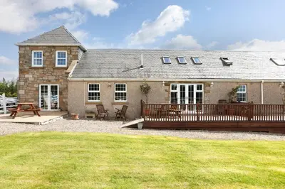 a house with a wooden deck and a patio at JOIVY Greenknowes Farmhouse with Hot Tub and Bar in Kelty