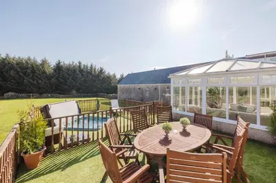 a patio with a table and chairs and a greenhouse at JOIVY Greenknowes Farmhouse with Hot Tub and Bar in Kelty