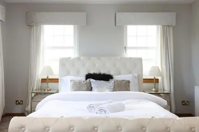 a bedroom with a large white bed with two windows at JOIVY Greenknowes Farmhouse with Hot Tub and Bar in Kelty