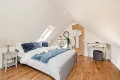 a white bedroom with a bed and a staircase at JOIVY Greenknowes Cottage with Hot Tub & Fireplace in Kelty