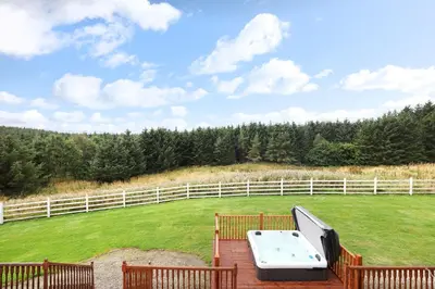 a deck with a table and a grill in a field at JOIVY Greenknowes Lodge with Hot Tub and Wood Burning Stove in Kelty