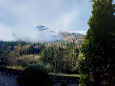 a snow covered mountain with trees and a road at An Carraig Log Cabin in Strathyre