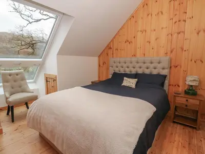 a bedroom with a large bed and a chair at Bradan Lodge in Dalmally