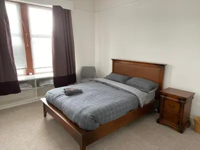 a bedroom with a bed and a table and two windows at Spacious 3 bedroom apartment in Campbeltown centre in Campbeltown