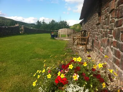 a garden with a bench and flowers next to a brick wall at Clan Cottages Luxury Thatched Retreat near Oban in Oban
