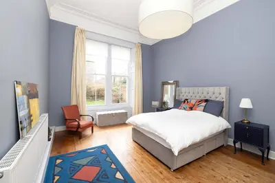 a bedroom with a bed and a chair and a window at JOIVY Spacious 2-Bedroom Ground Floor Flat in Edinburgh