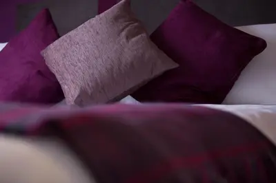 a pile of pillows on a bed with purple pillows at The Spires Serviced Apartments Edinburgh in Edinburgh