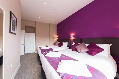 two beds in a hotel room with purple walls at The Spires Serviced Apartments Edinburgh in Edinburgh