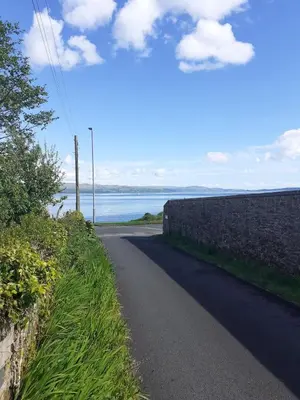 a road next to a wall next to the ocean at The Snug a cosy, quirky detached cottage with sea views in Innellan