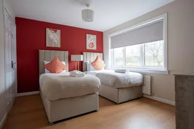 two beds in a bedroom with red walls and a window at Beauly Court Suites in Grangemouth