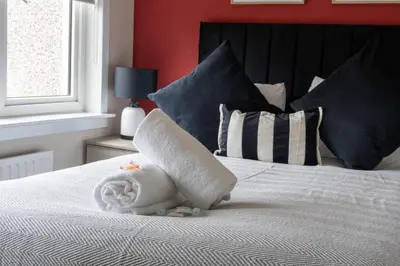 a white bed with pillows and a towel on it at Beauly Court Suites in Grangemouth