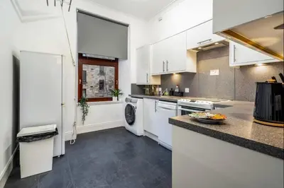 a kitchen with white cabinets and a washer and dryer at Cheerful 1 Bedroom Homely Apartment, Sleeps 4 Guest Comfy, 1 x Double Bed, 1 x Sofa Bed, Parking, Free WiFi, Suitable For Business, Leisure Guest,Glasgow, Glasgow West End, Near City Centre, Perfect for Common Wealth Games 2026 in Glasgow