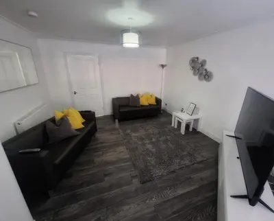 a living room with a black couch and yellow pillows at Cozy Shotts House with 2 Bedrooms in Kirk of Shotts