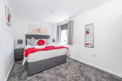 a white bedroom with a large bed with red pillows at Super Prime Luxury 4 Bedroom Detached Home by TBA in Fife