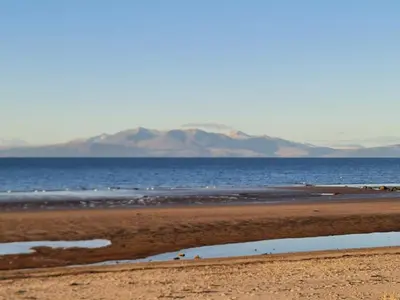 a beach with a body of water and mountains in the background at The Old High Road, North Ayrshire in Stevenston