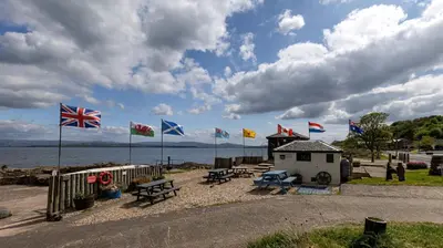 a group of flags on a beach with benches at Coastal Charm in Kingarth
