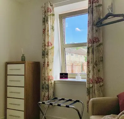 a bedroom with a window and a chair and a dresser at Cottage in Mid Calder Village near Edinburgh in Mid Calder