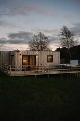 a wooden house with a deck in a field at The Byre, Summerhill Farm Stays in Balmaclellan