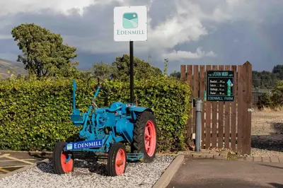 a blue tractor is parked next to a sign at Edenmill Farm in Glasgow