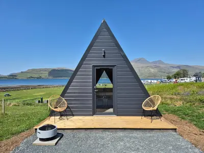 a black triangular house with two chairs and a stove at The Hideouts at Port nan Gael Campsite in Pennyghael