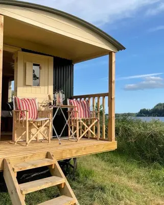 a house with a deck with chairs and a table at The Secret Shepherds Hut- Off Grid Retreat in New Galloway