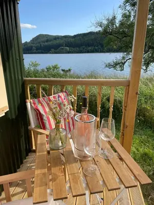 a wooden table with wine glasses and a view of the water at The Secret Shepherds Hut- Off Grid Retreat in New Galloway