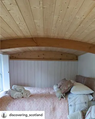 a bed in a room with a wooden ceiling at The Hidden Shepherds Hut- Off Grid Retreat in Castle Douglas