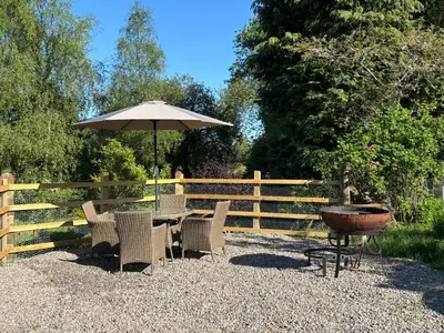 a table and chairs with an umbrella and a grill at The Bothy, Callander in Callander