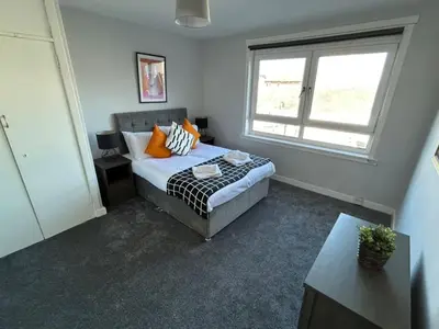 a bedroom with a bed with orange pillows and a window at 3-Bed Apartment Central Greenock in Greenock