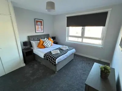 a bedroom with a bed with orange pillows and a window at 3-Bed Apartment Central Greenock in Greenock