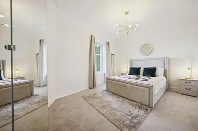 a white bedroom with a bed and a mirror at Large Terraced Home with Parking in Glasgow