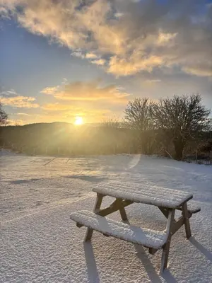 a bench sitting in the snow with the sun in the background at The Pods at 7 Black Crofts in Oban
