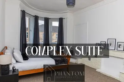 a bedroom with a bed with black curtains and a window at Complexx Suite in Glasgow