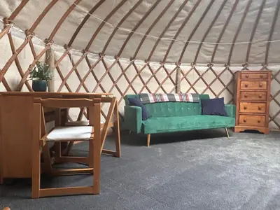 a green couch in a yurt with a table and a chair at Bracken Barns Glamping & Massage in Minishant