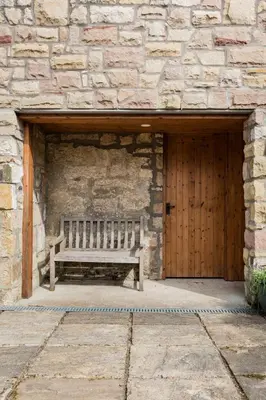 a wooden bench in front of a stone building with a wooden door at Converted Historical Stone Coach House in Glasgow