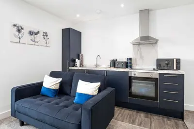 a living room with a blue couch in front of a kitchen at Modern & Central 1BR Flat with Sky TV in Oban
