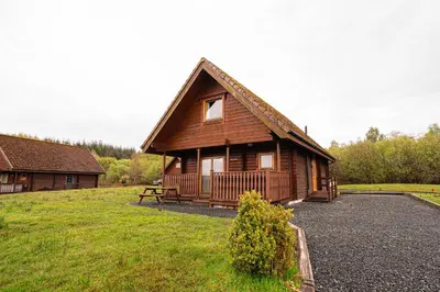a large wooden cabin with a bench in front of it at Lodge 1 in Stirling