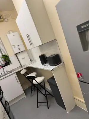 a small kitchen with white cabinets and a counter with stools at Cozy Central 1 Min to Tube in Moffat