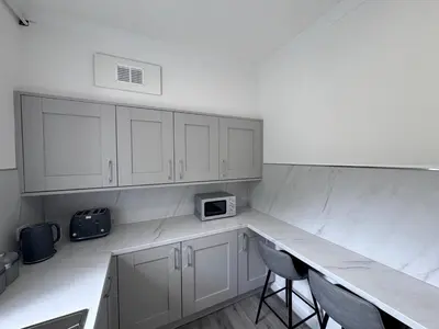 a kitchen with white cabinets and a counter with chairs at Helensburgh Central Apartment - Macaulay Letting in Helensburgh