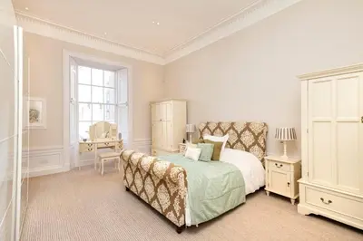 a white bedroom with a bed and a chair at Melville Street Townhouse in Edinburgh