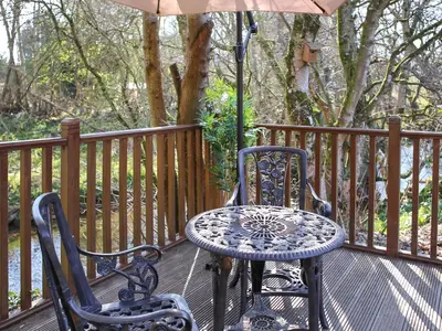 a table and chairs on a deck with an umbrella at Burnside Lodge in Auchterarder