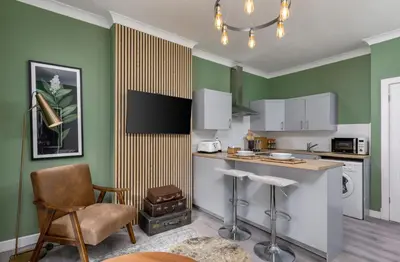 a kitchen with green walls and a counter and chairs at Ochill View Apartment by Stirling Train Station in Stirling