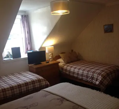a bedroom with two beds and a computer on a desk at Tanglin Guest House in Oban