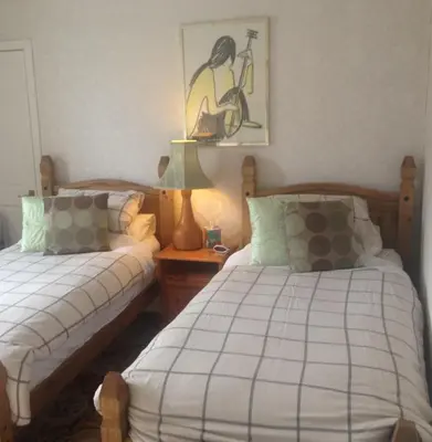 a bedroom with two beds and a table with a lamp at Tanglin Guest House in Oban