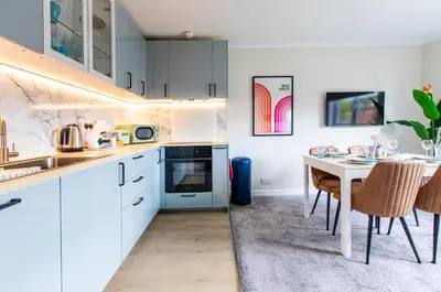 a kitchen with white cabinets and a table with chairs at John Neilson View - Coorie Doon in Paisley