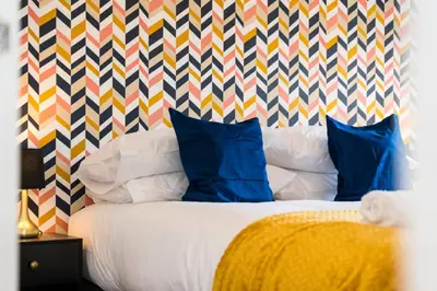 a bed with blue pillows and a colorful patterned wall at Macallan Apartment in Oban