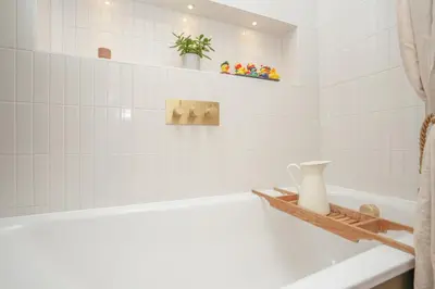 a white bathroom with a tub and a vase on a shelf at Luxury Wood panelled West End GF Flat in Edinburgh