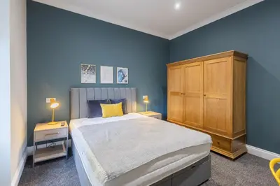 a blue bedroom with a large bed and a wooden cabinet at 3BR Gem West End Walk to Glasgow Uni Parking in Glasgow