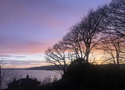 a sunset over a body of water with trees at Cliff Top - Bubbling Springs in Wemyss Bay